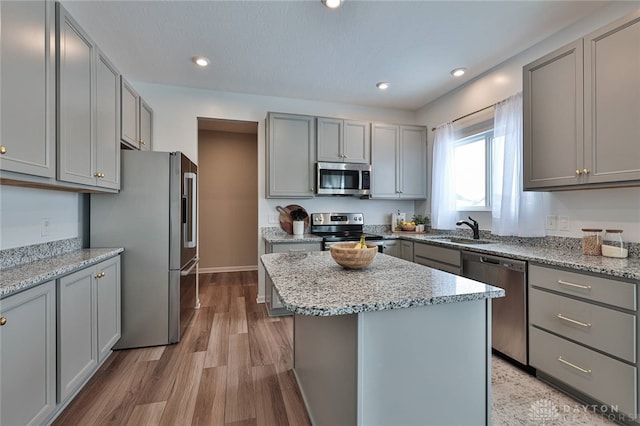 kitchen with light stone counters, a center island, stainless steel appliances, gray cabinets, and a sink