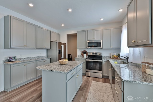 kitchen with a kitchen island, appliances with stainless steel finishes, gray cabinets, and light stone counters