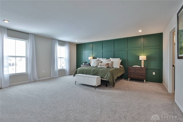 bedroom with recessed lighting, light colored carpet, a decorative wall, a textured ceiling, and baseboards