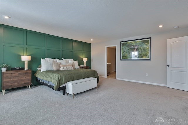 bedroom featuring recessed lighting, light colored carpet, a decorative wall, and baseboards