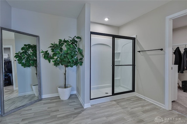 bathroom with a walk in closet, a shower stall, baseboards, and wood finished floors