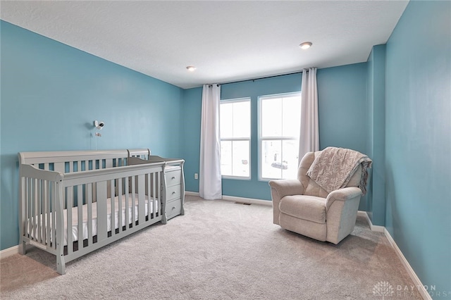 bedroom featuring light carpet, a crib, visible vents, and baseboards