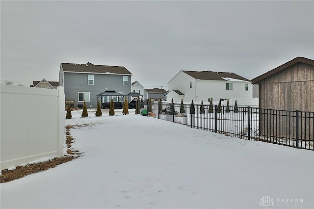 snowy yard featuring a gazebo, fence, and a residential view