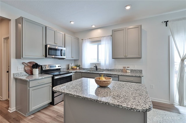 kitchen featuring light stone counters, stainless steel appliances, a sink, a kitchen island, and gray cabinets