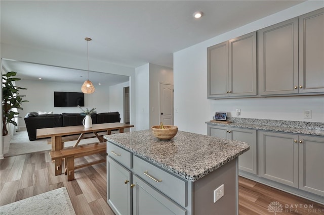 kitchen featuring a kitchen island, open floor plan, decorative light fixtures, light stone countertops, and gray cabinetry