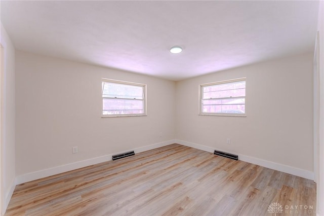 empty room featuring baseboards, visible vents, and light wood finished floors