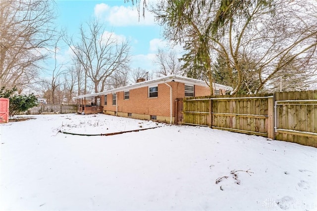 snow covered house featuring brick siding, a chimney, and fence