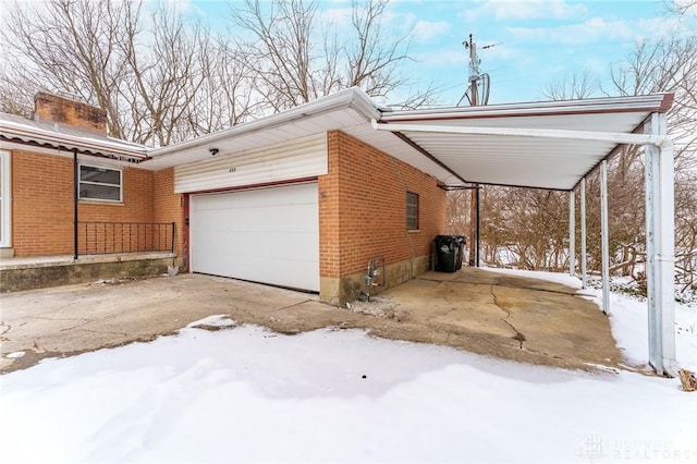 view of snow covered exterior featuring a garage, a carport, brick siding, and driveway