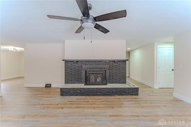 unfurnished living room featuring light wood-type flooring, a wood stove, ceiling fan, and baseboards