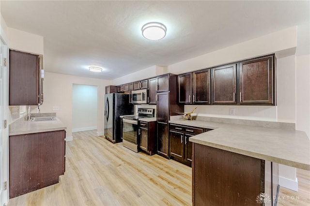 kitchen with a breakfast bar area, light countertops, appliances with stainless steel finishes, a sink, and dark brown cabinets