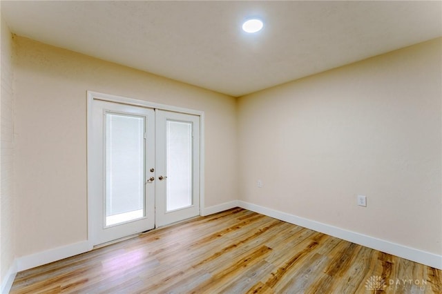 spare room featuring french doors, light wood-style flooring, and baseboards