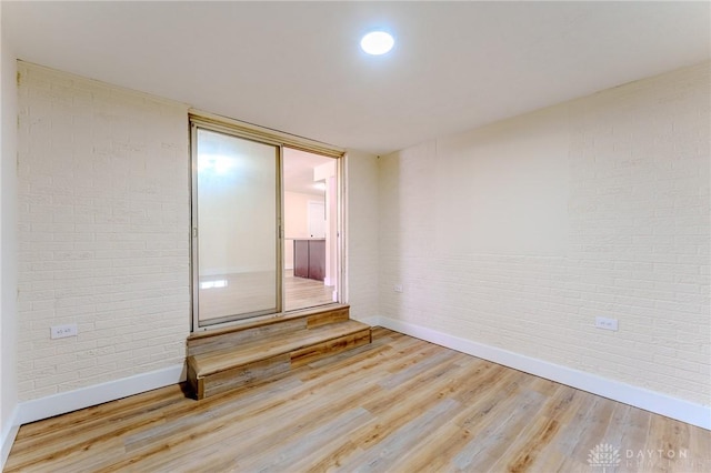 empty room featuring light wood-type flooring, brick wall, and baseboards