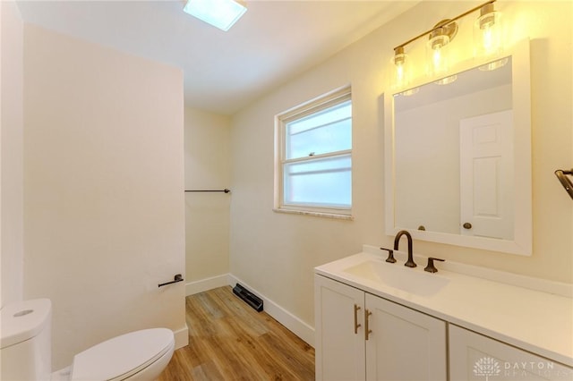 half bathroom with baseboards, visible vents, toilet, wood finished floors, and vanity