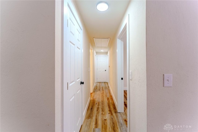 hallway featuring light wood-type flooring, attic access, baseboards, and a textured wall