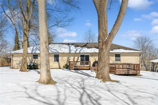 snow covered property with brick siding, fence, and a deck