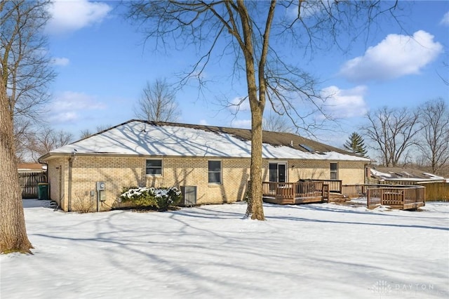 snow covered house with brick siding, fence, and a wooden deck