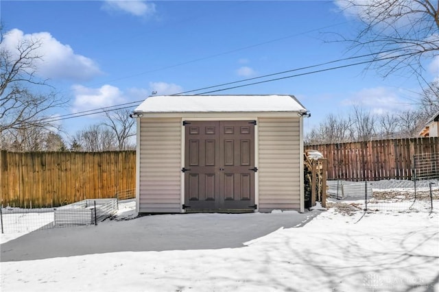 snow covered structure featuring a storage unit, an outdoor structure, and fence