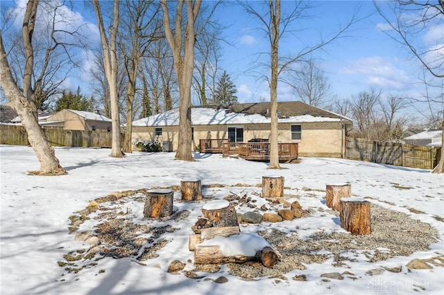 snow covered rear of property with brick siding, a wooden deck, and fence