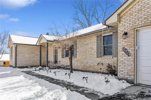 view of snow covered exterior featuring a garage and brick siding