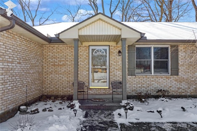 snow covered property entrance with brick siding