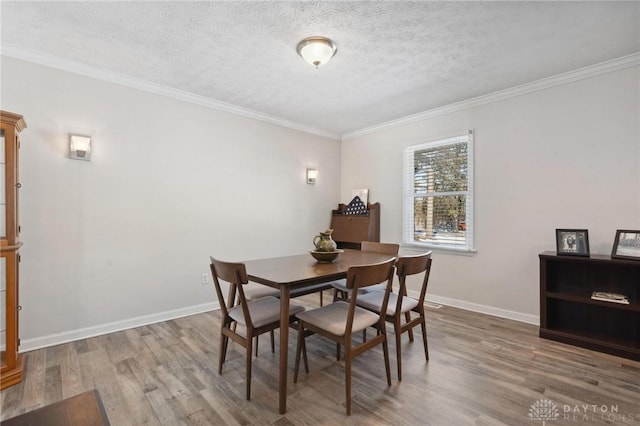 dining space with ornamental molding, a textured ceiling, baseboards, and wood finished floors