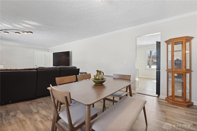 dining area featuring light wood finished floors, crown molding, baseboards, and a textured ceiling