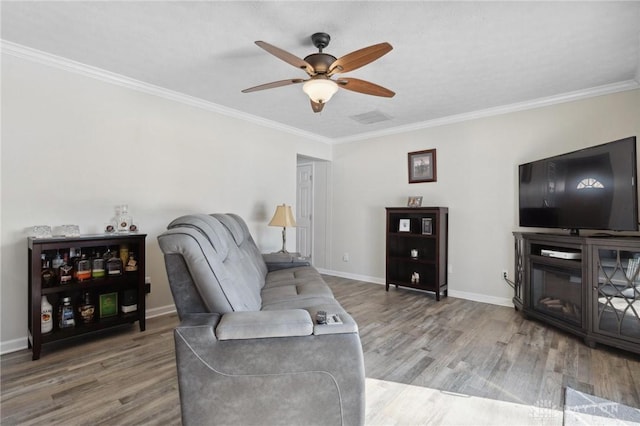 living area featuring a ceiling fan, crown molding, baseboards, and wood finished floors