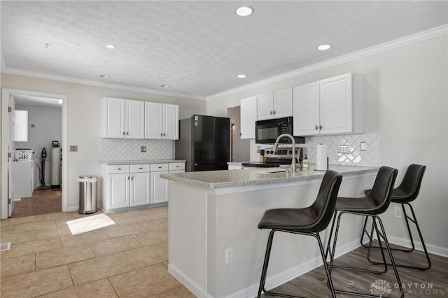 kitchen with a kitchen breakfast bar, a peninsula, light countertops, black appliances, and white cabinetry