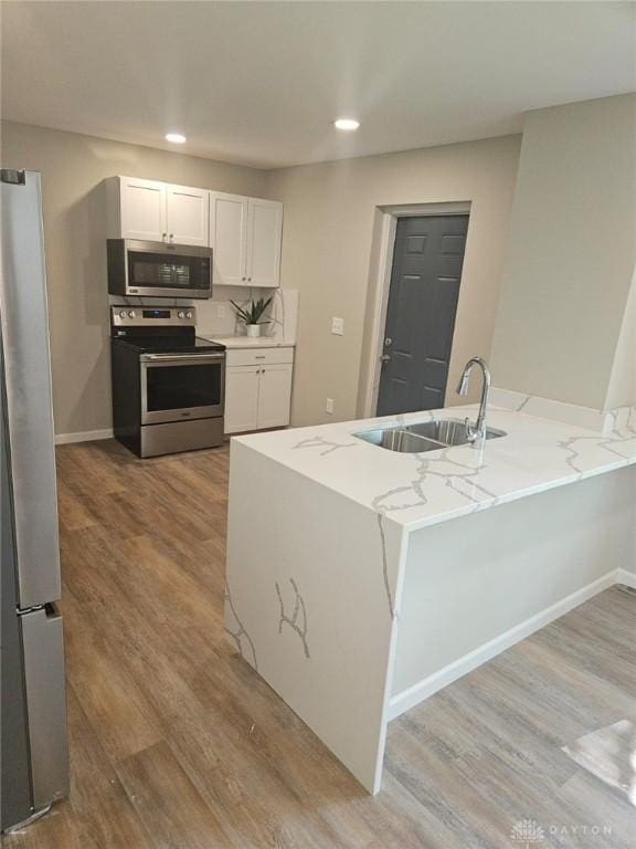 kitchen featuring a peninsula, a sink, white cabinetry, appliances with stainless steel finishes, and light stone countertops