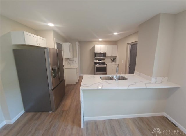 kitchen with appliances with stainless steel finishes, white cabinets, a sink, light wood-type flooring, and a peninsula