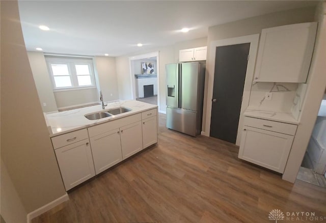 kitchen featuring dark wood-style flooring, a fireplace, white cabinets, a sink, and stainless steel fridge