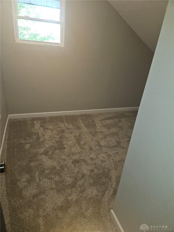 carpeted empty room with vaulted ceiling and baseboards