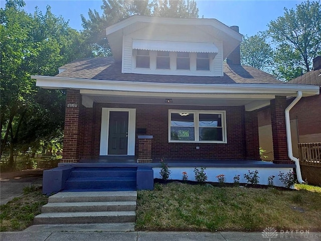 bungalow-style house featuring a porch, a shingled roof, and brick siding