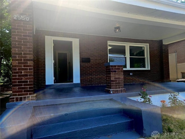 entrance to property featuring a porch and brick siding