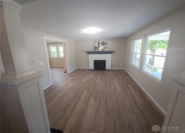 unfurnished living room featuring baseboards, dark wood-style flooring, a brick fireplace, and ornate columns