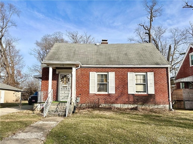 view of front facade with brick siding, a front lawn, a chimney, and a shingled roof