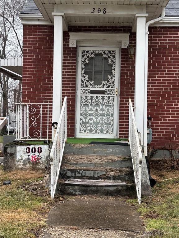 doorway to property with a shingled roof and brick siding