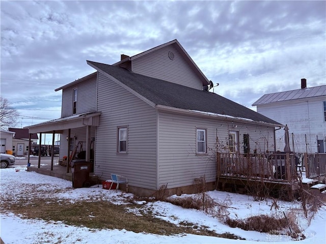 view of snow covered exterior with roof with shingles and a deck