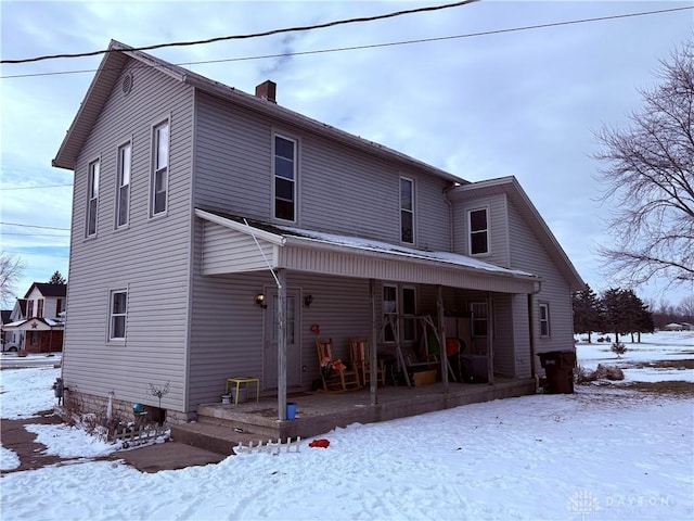 snow covered back of property with a porch and a chimney