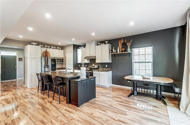 kitchen featuring light wood-style flooring, a breakfast bar, a kitchen island with sink, stainless steel appliances, and white cabinetry