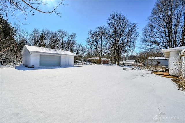 yard layered in snow featuring a detached garage and an outdoor structure