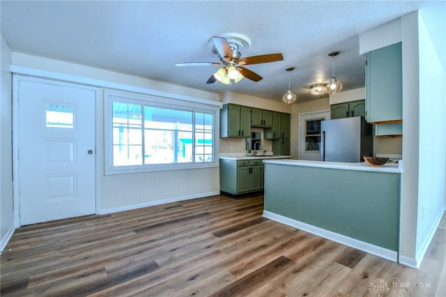 kitchen featuring light countertops, green cabinets, freestanding refrigerator, wood finished floors, and a peninsula