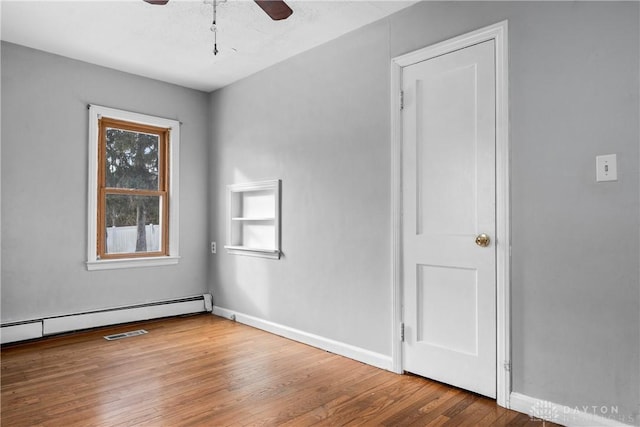 empty room with a ceiling fan, a baseboard radiator, baseboards, and wood finished floors