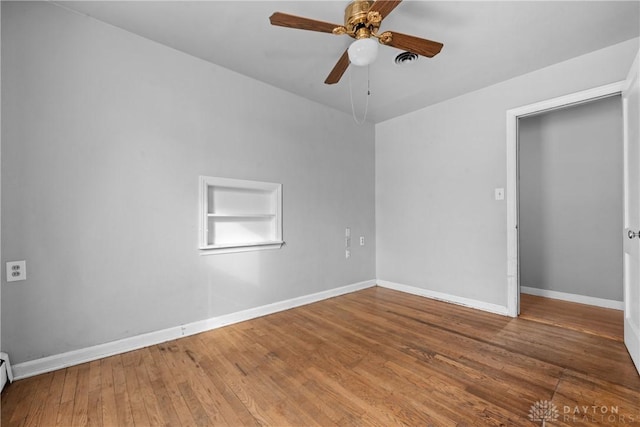 unfurnished room with ceiling fan, a baseboard heating unit, wood finished floors, visible vents, and baseboards