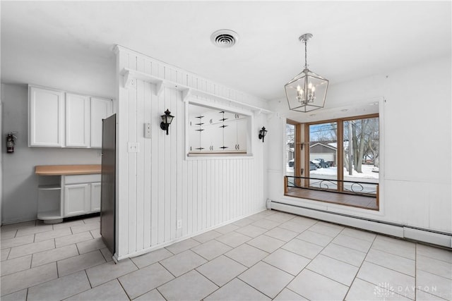 unfurnished dining area featuring light tile patterned floors, visible vents, baseboard heating, and a chandelier