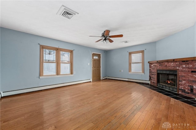 unfurnished living room with a baseboard heating unit, a brick fireplace, visible vents, and wood finished floors