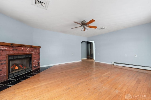 unfurnished living room featuring arched walkways, visible vents, baseboard heating, a brick fireplace, and wood finished floors