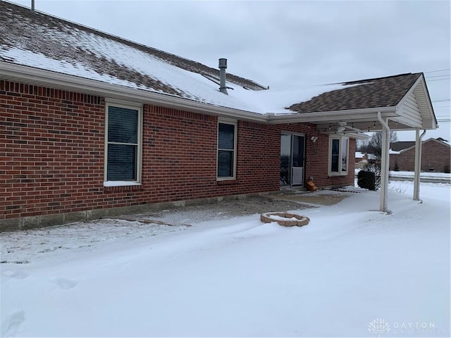 snow covered rear of property featuring brick siding