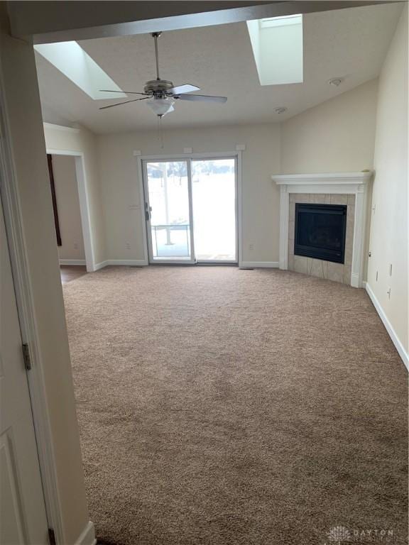 unfurnished living room featuring vaulted ceiling with skylight, a tile fireplace, light carpet, a ceiling fan, and baseboards