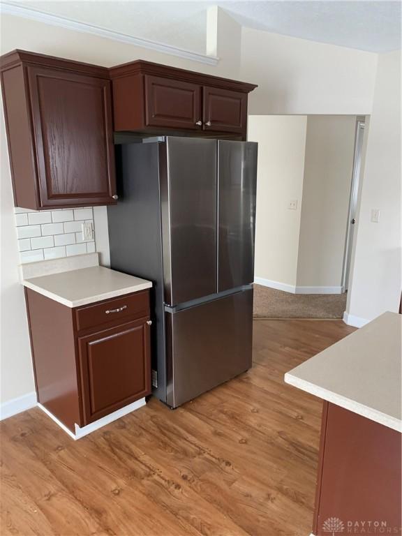 kitchen featuring baseboards, light countertops, light wood-type flooring, backsplash, and freestanding refrigerator